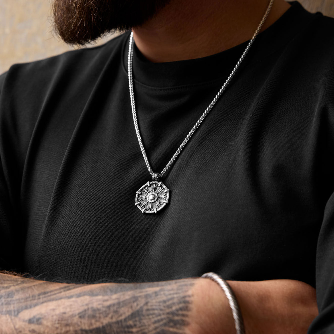 Helm of Awe necklace worn by tattooed man, showing Norse shield pendant with protection symbol on rugged Viking-style chain.