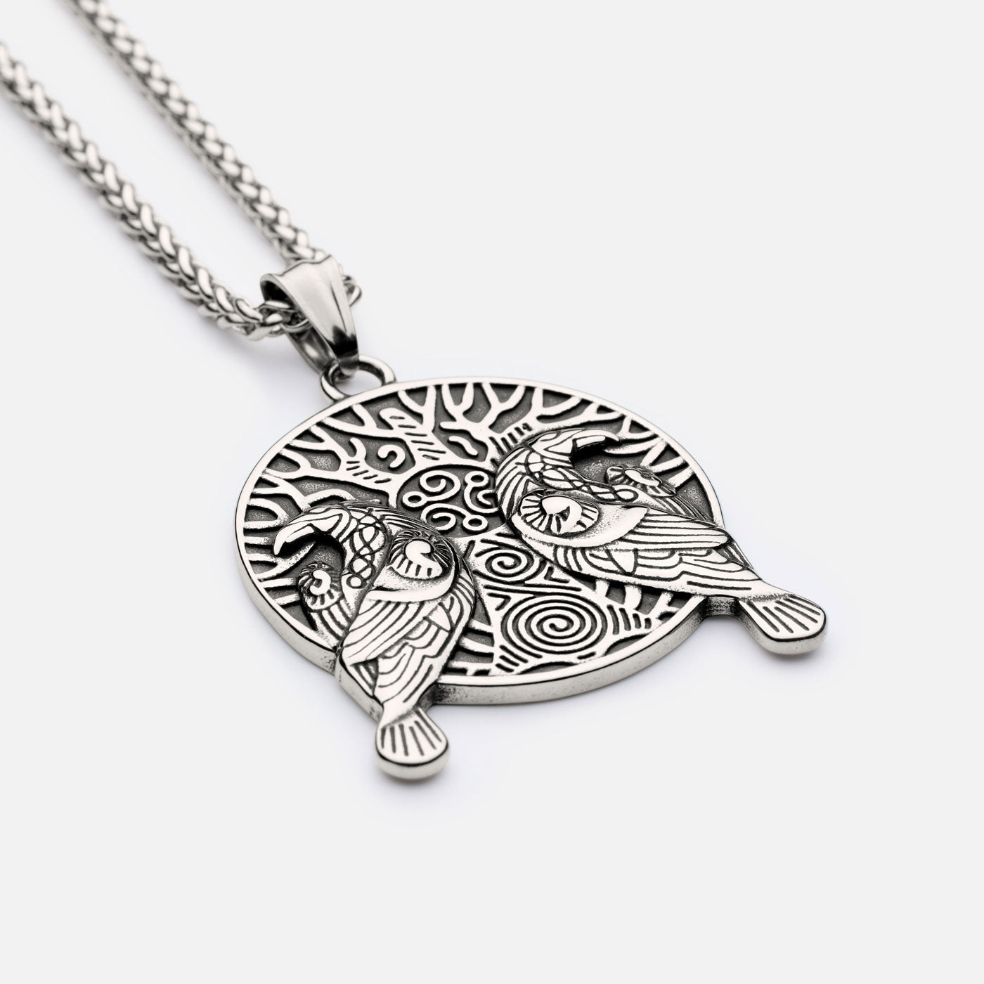 Side view of Norse raven pendant showing Hugin and Munin resting on Yggdrasil with engraved Viking spiral patterns.