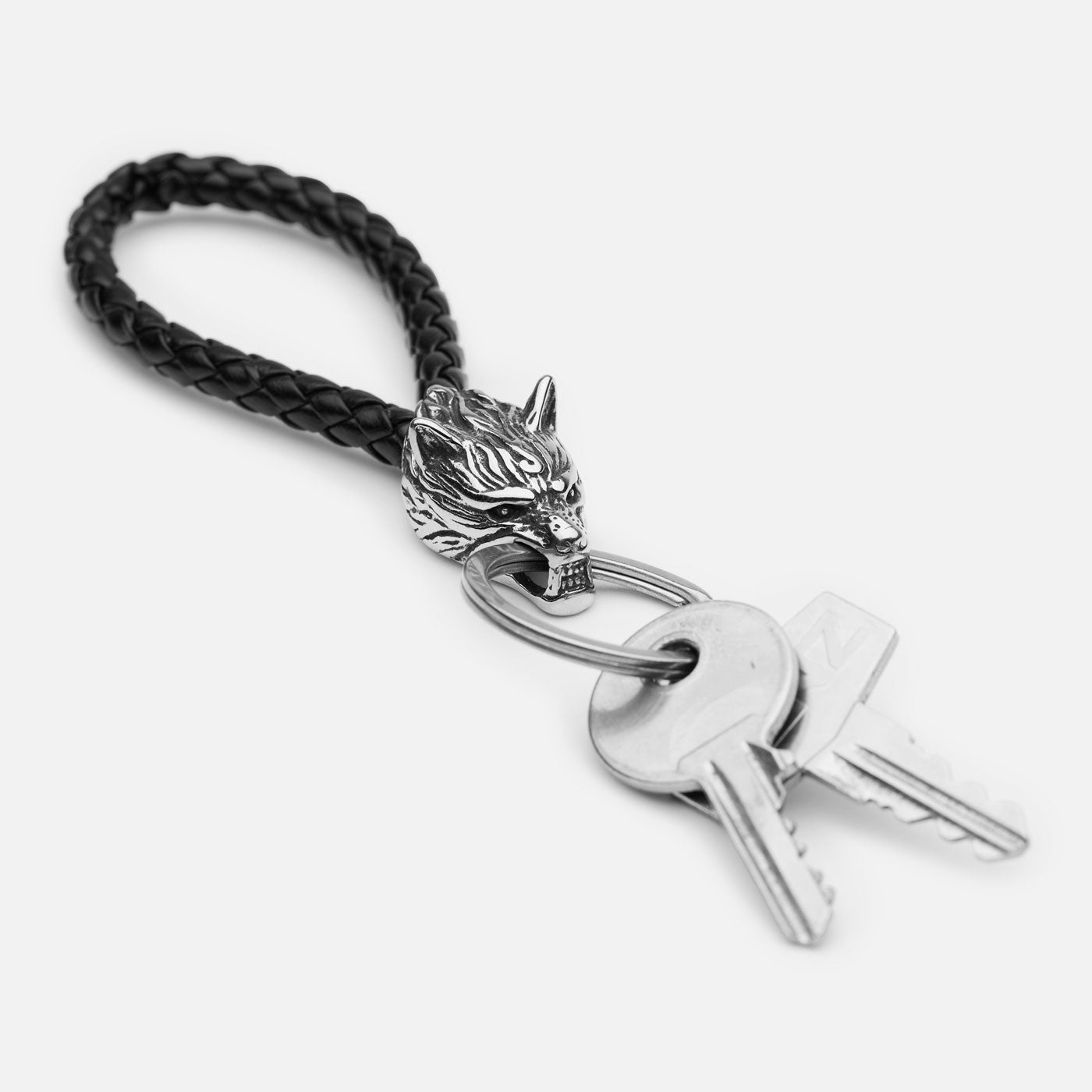 Detailed wolf head keychain on braided black leather strap with stainless steel ring and keys attached, studio shot on white.