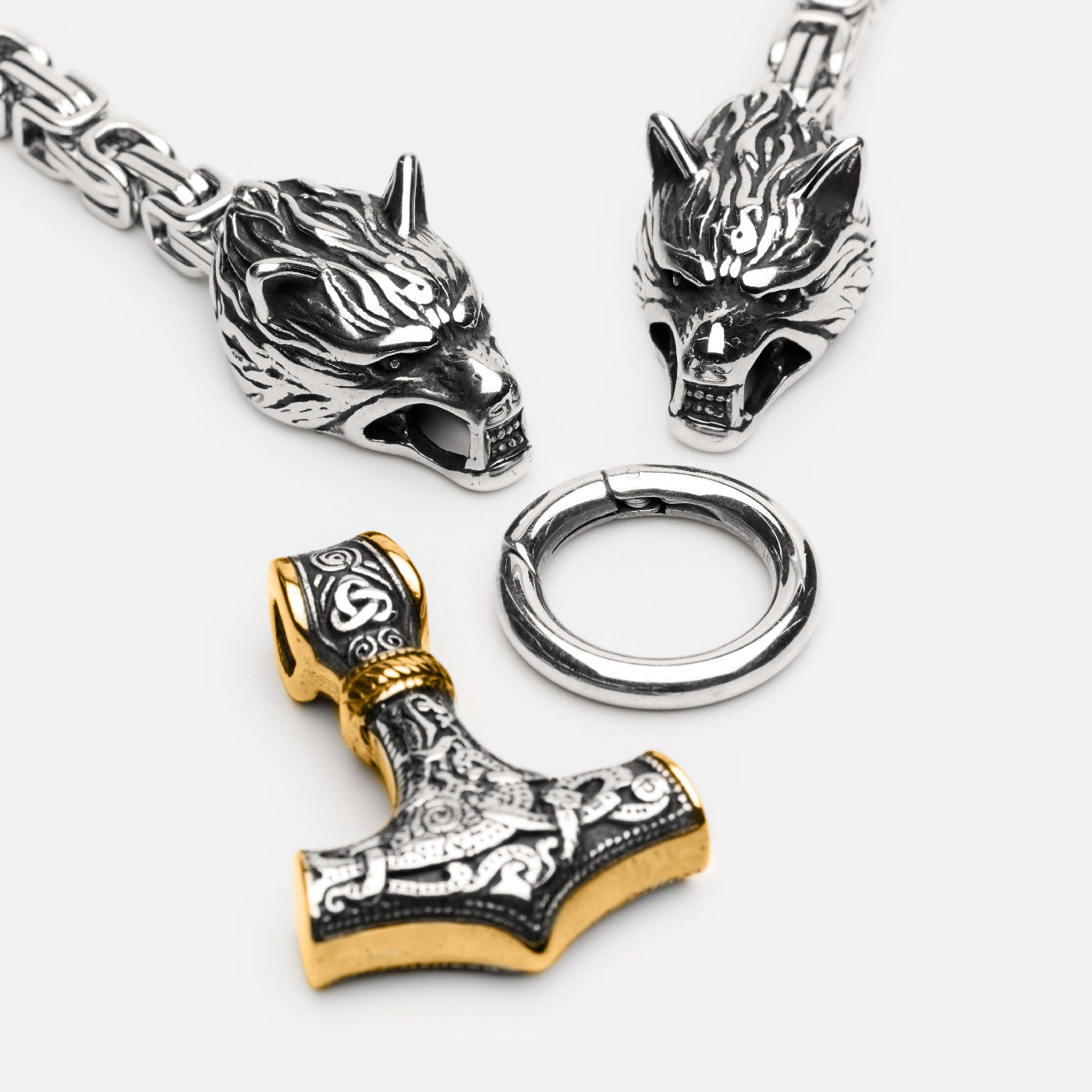 Close-up of Norse King’s Chain necklace featuring two detailed wolf heads and a detachable gold-accented Mjölnir pendant.