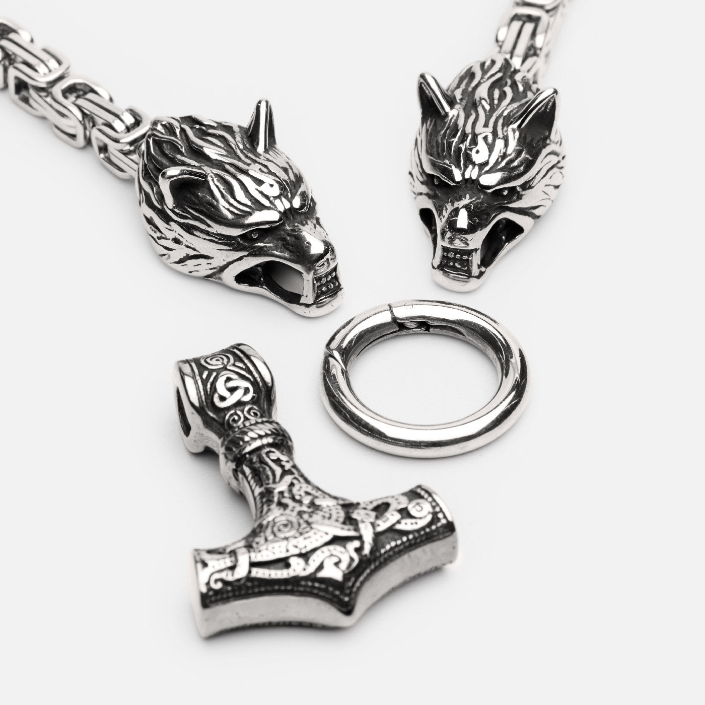 Close-up of Norse King’s Chain necklace featuring two detailed wolf heads and a detachable silver-accented Mjölnir pendant.
