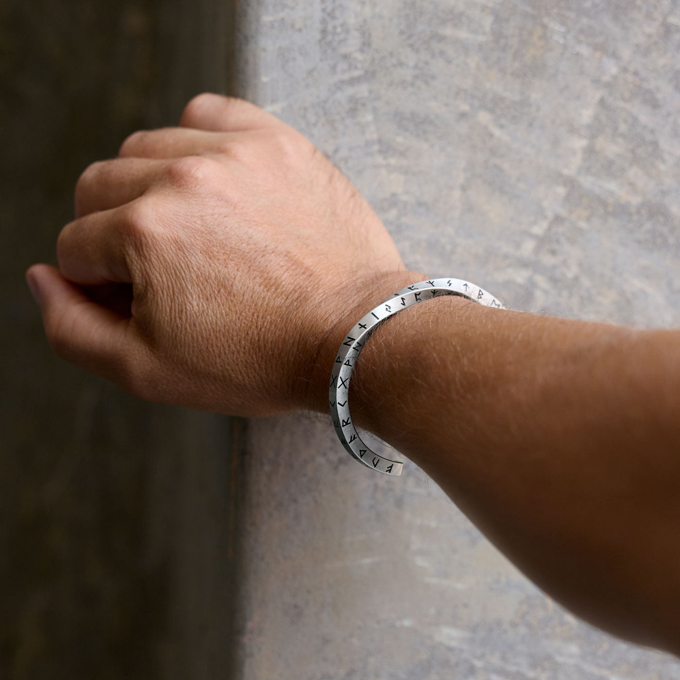 Elder Futhark Rune Bracelet worn on a wrist, showcasing the ancient Norse runes deeply engraved into the silver stainless steel Viking cuff.