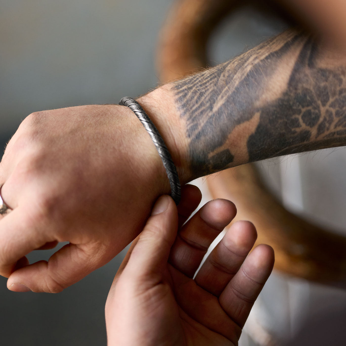 A Viking-style wolf bracelet worn on a wrist, featuring intricately designed wolf heads on both ends. The detailed bracelet coils around the wrist, displaying strong craftsmanship and a tattooed arm.