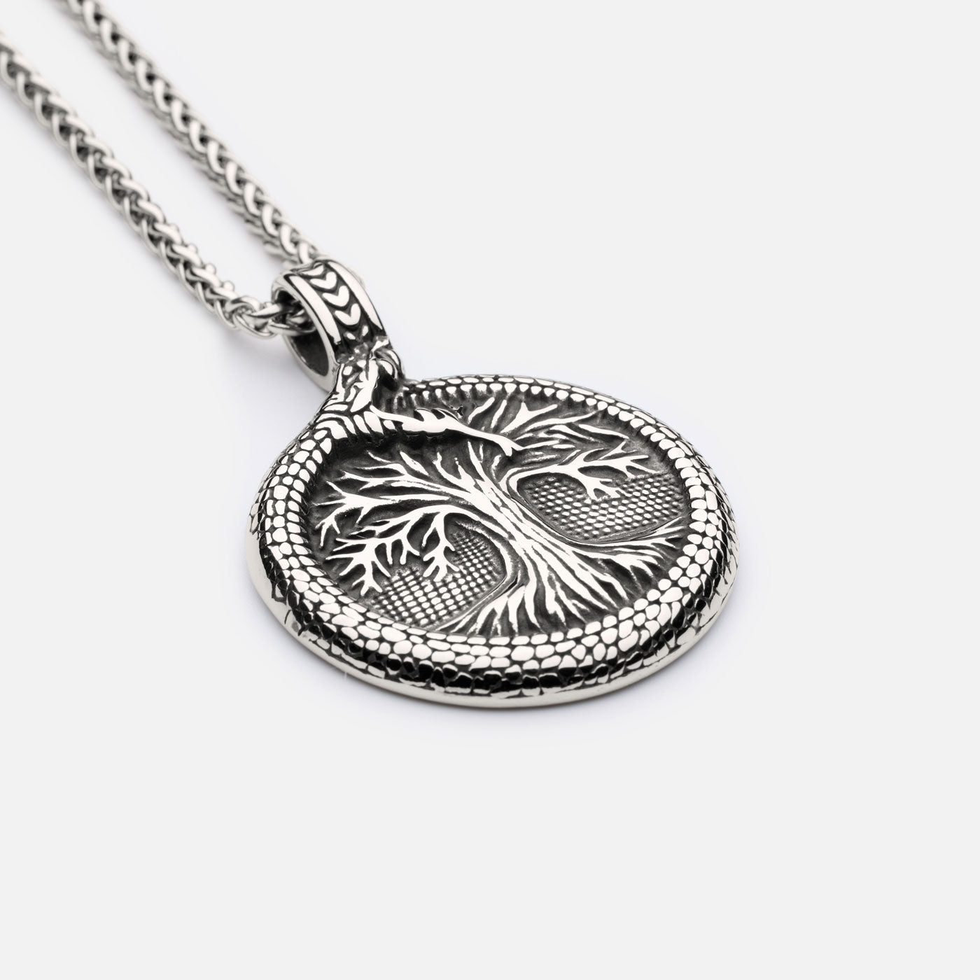 Close-up of Yggdrasil pendant with serpent Jormungandr biting its tail, symbolizing Norse eternity and Viking belief.