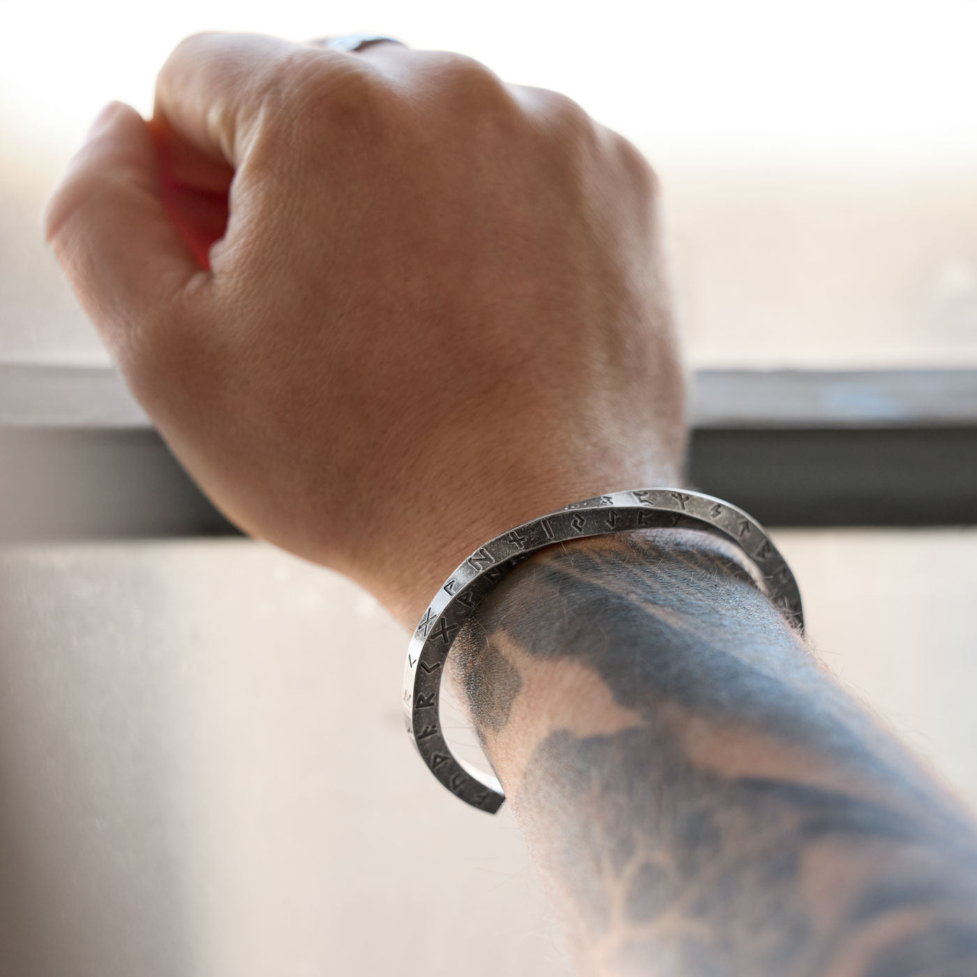 Elder Futhark Rune Bracelet worn on a tattooed wrist, showcasing the ancient Norse runes deeply engraved into the rugged stainless steel Viking cuff.
