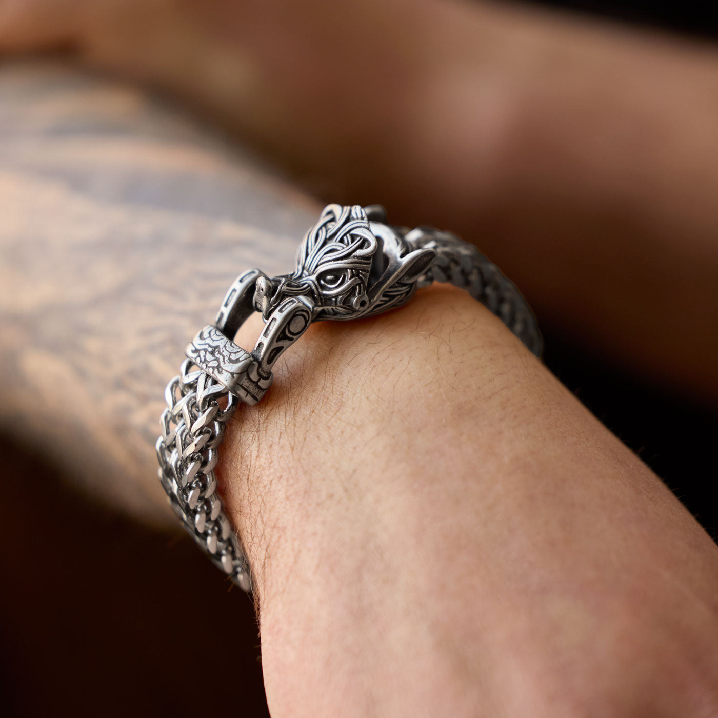 A stainless steel Fenrir wolf bracelet from Odin Trinkets worn on a tattooed wrist, highlighting its bold Norse-inspired design and powerful symbolism.