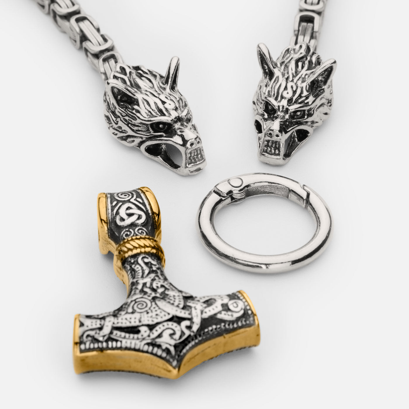 Disassembled view of the stainless steel Mjölnir pendant in gold and silver from Odin Trinkets, showcasing the detailed Thor’s hammer, Geri & Freki wolf head clasps, and the sturdy Viking ring connector.