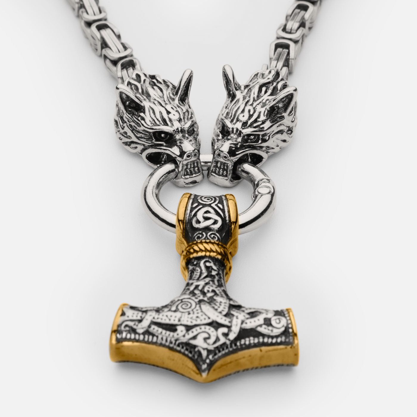 Close-up of the stainless steel Mjölnir pendant in gold and silver from Odin Trinkets, featuring intricate Norse engravings, a bold Viking hammer design, and Geri & Freki wolf heads gripping the ring.