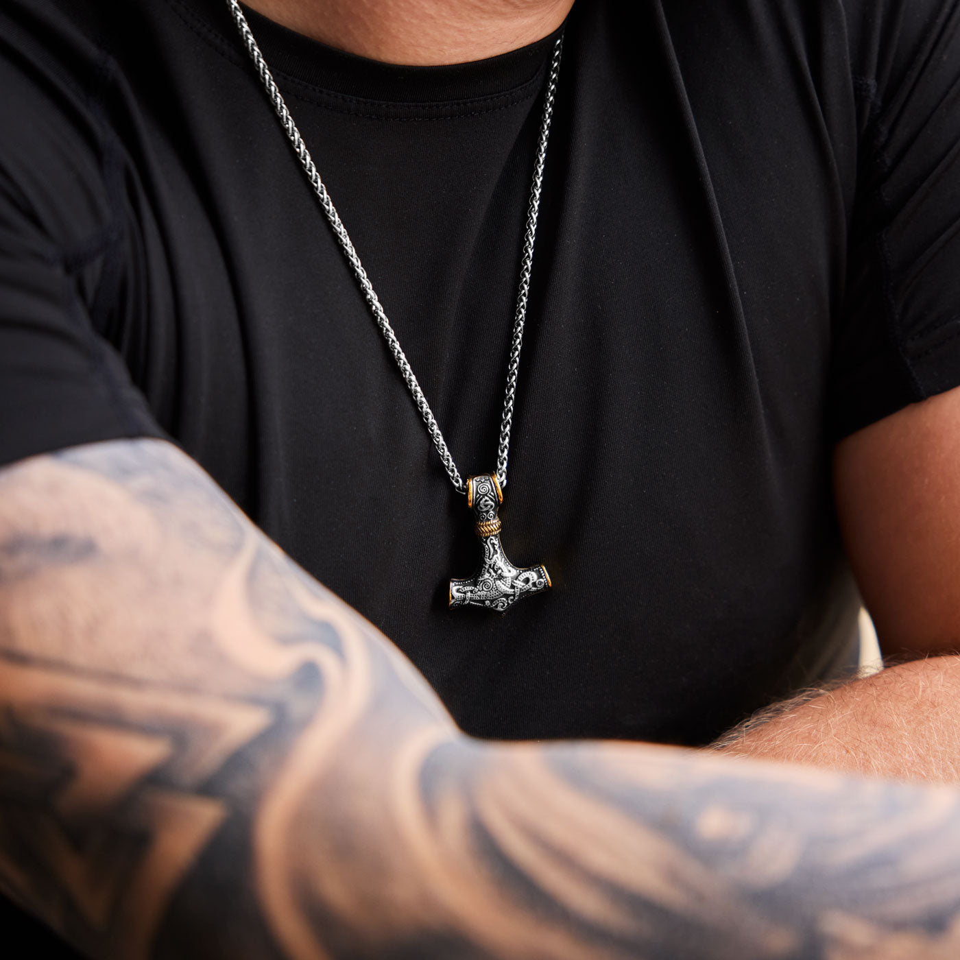 The stainless steel Mjölnir pendant in gold and silver from Odin Trinkets, worn on a simple Viking chain, featuring intricate Norse engravings for a bold warrior look.