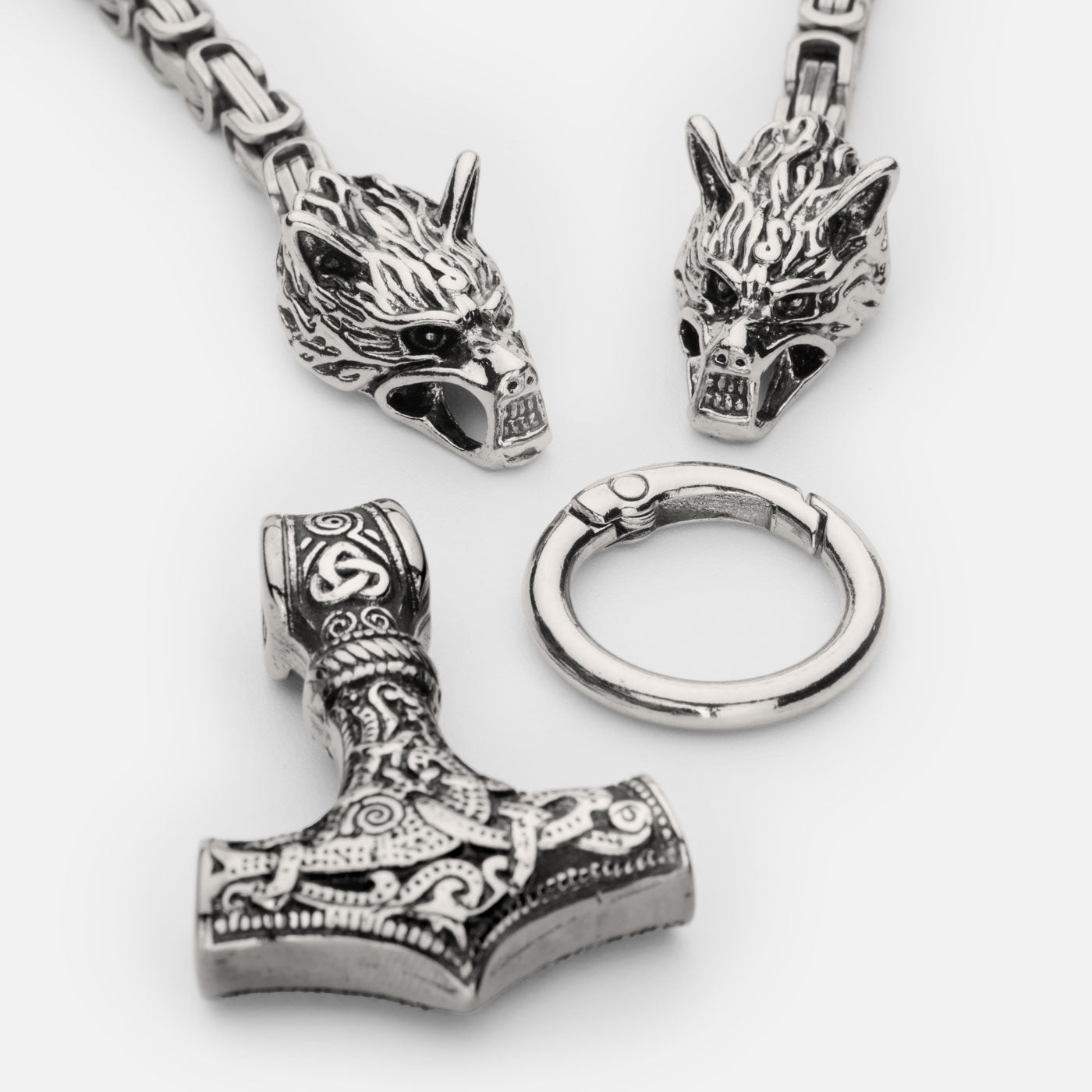 Disassembled view of the stainless steel Mjölnir pendant in silver from Odin Trinkets, showcasing the detailed Thor’s hammer, Geri & Freki wolf head clasps, and the sturdy Viking ring connector.