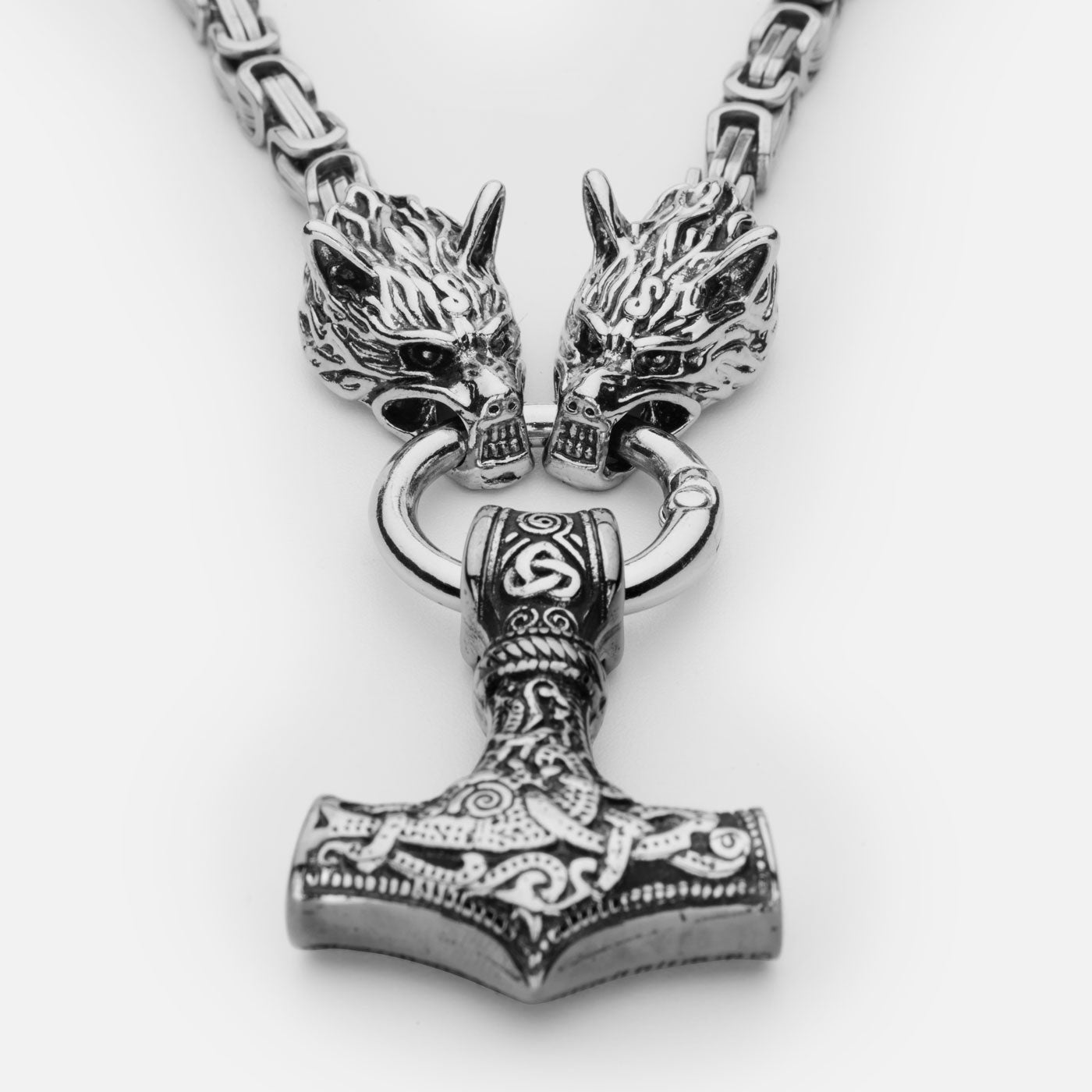Close-up of the stainless steel Mjölnir pendant in silver from Odin Trinkets, featuring intricate Norse engravings, a bold Viking hammer design, and Geri & Freki wolf heads gripping the ring.