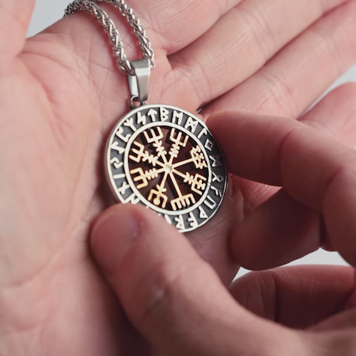 Close-up video of a stainless steel Vegvísir necklace, featuring gold-accented details and surrounded by Elder Futhark runes. This Viking compass pendant is a powerful Norse symbol of protection and guidance. Designed for those who seek their path—crafted with precision by Odin Trinkets.
