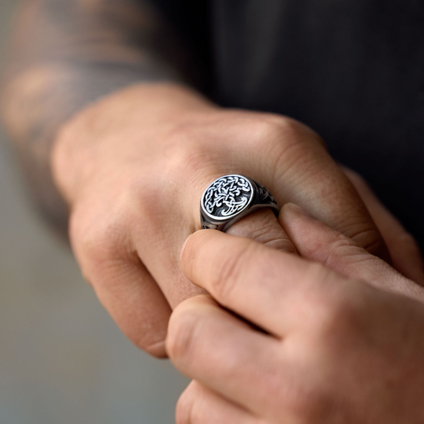 A close-up view of a person wearing the Yggdrasil ring, showing the intricate knotwork design on the ring's face, with the person’s fingers gently resting on their other hand.