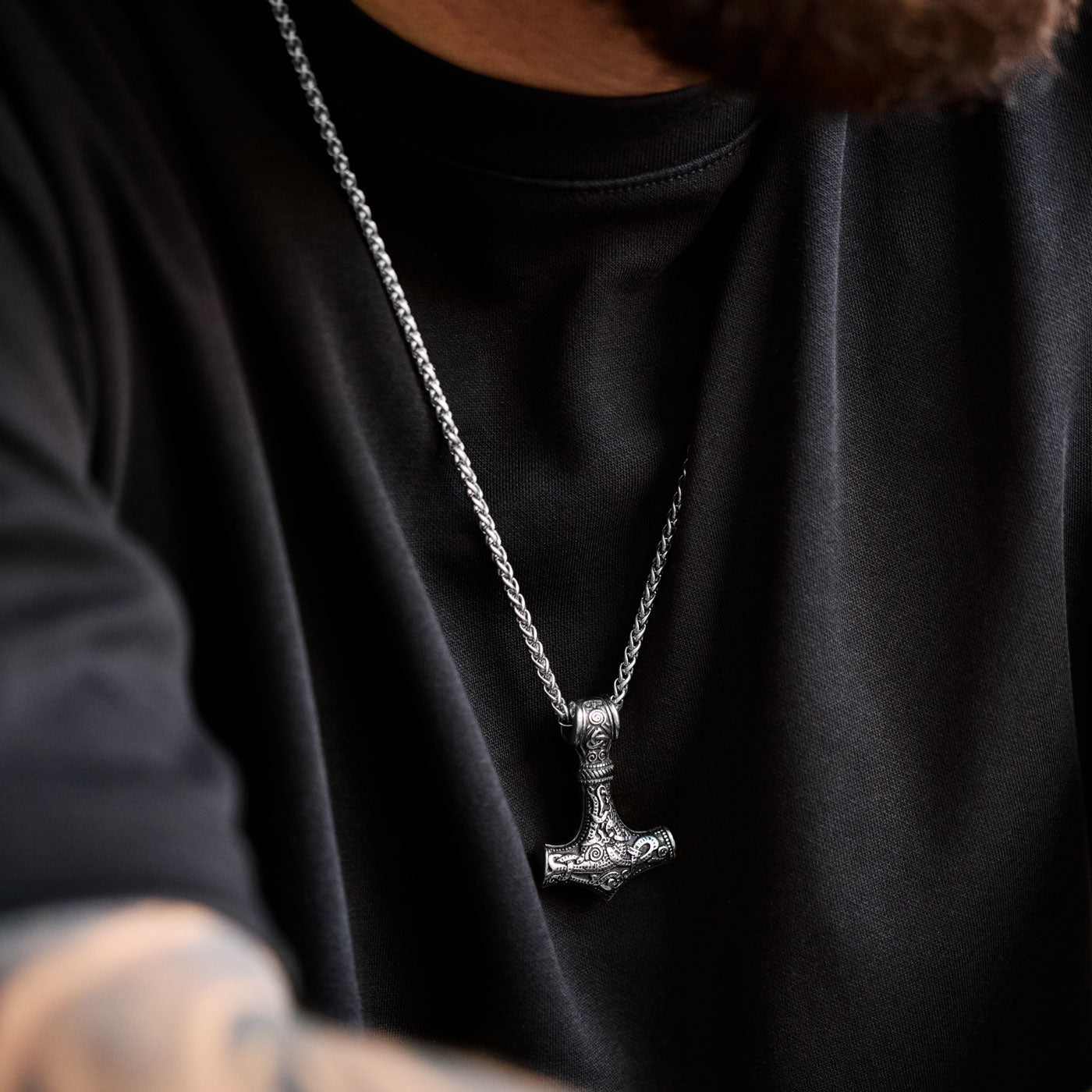 The stainless steel Mjölnir pendant in silver from Odin Trinkets, worn on a simple Viking chain, featuring intricate Norse engravings for a bold warrior look.