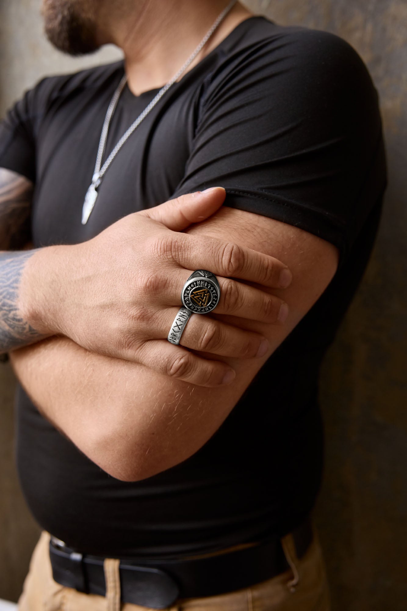 Man wearing a silver Valknut ring with gold accents alongside a rune-engraved sterling silver ring, styled with a casual black shirt and beige trousers, showcasing Norse-inspired accessories.