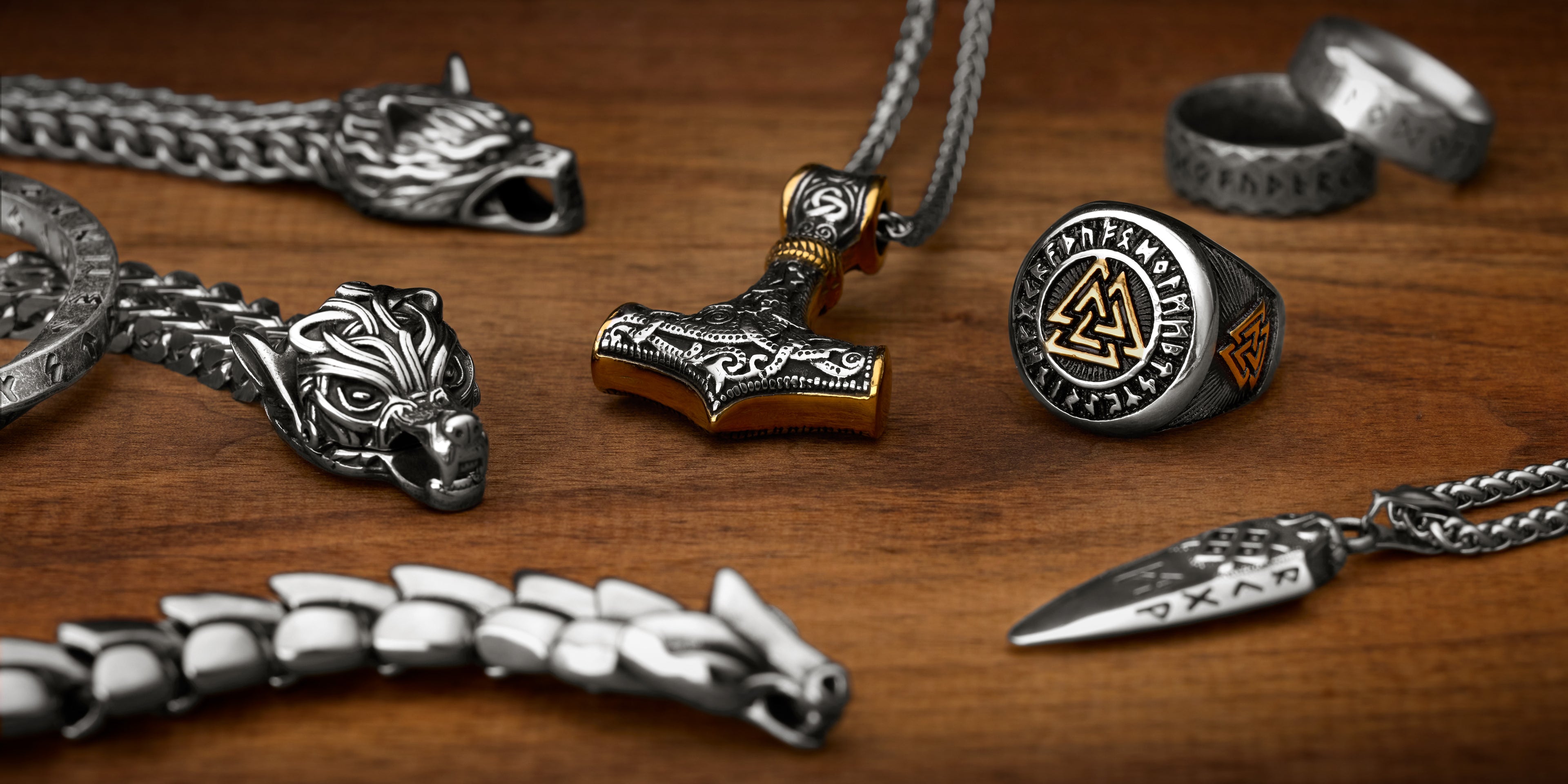 Norse mythology-inspired jewelry on wood, featuring a Thor's Hammer pendant, a Valknut ring with Elder Futhark runes, wolf head bracelet, rune rings, and a rune necklace, showcasing Viking strength and mysticism.