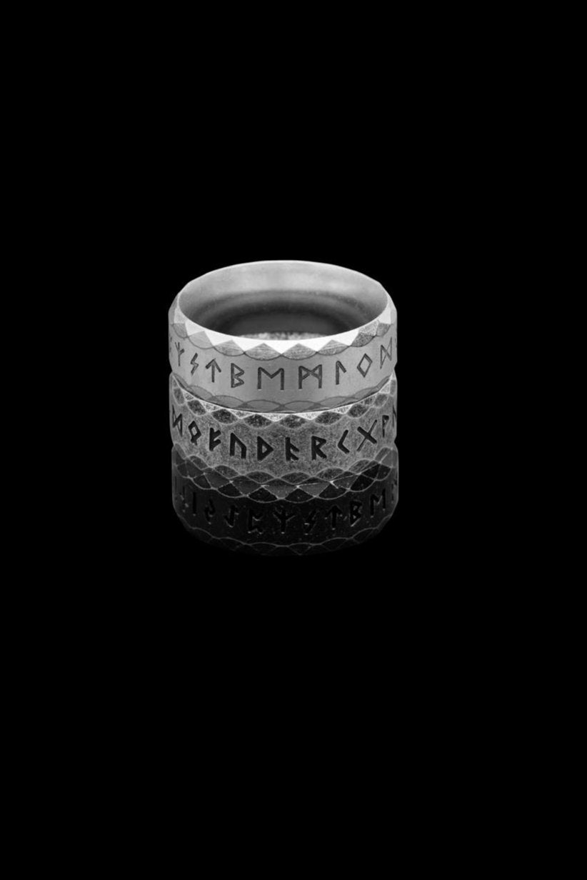 Three stainless steel rune rings engraved with the complete Elder Futhark alphabet, stacked in a gradient display. The top ring, labeled "Silver," features a polished metallic finish. The middle ring, the "Retro" variation, has a textured gray surface. The bottom ring, called "Antique," displays a matte black design, creating a striking contrast.