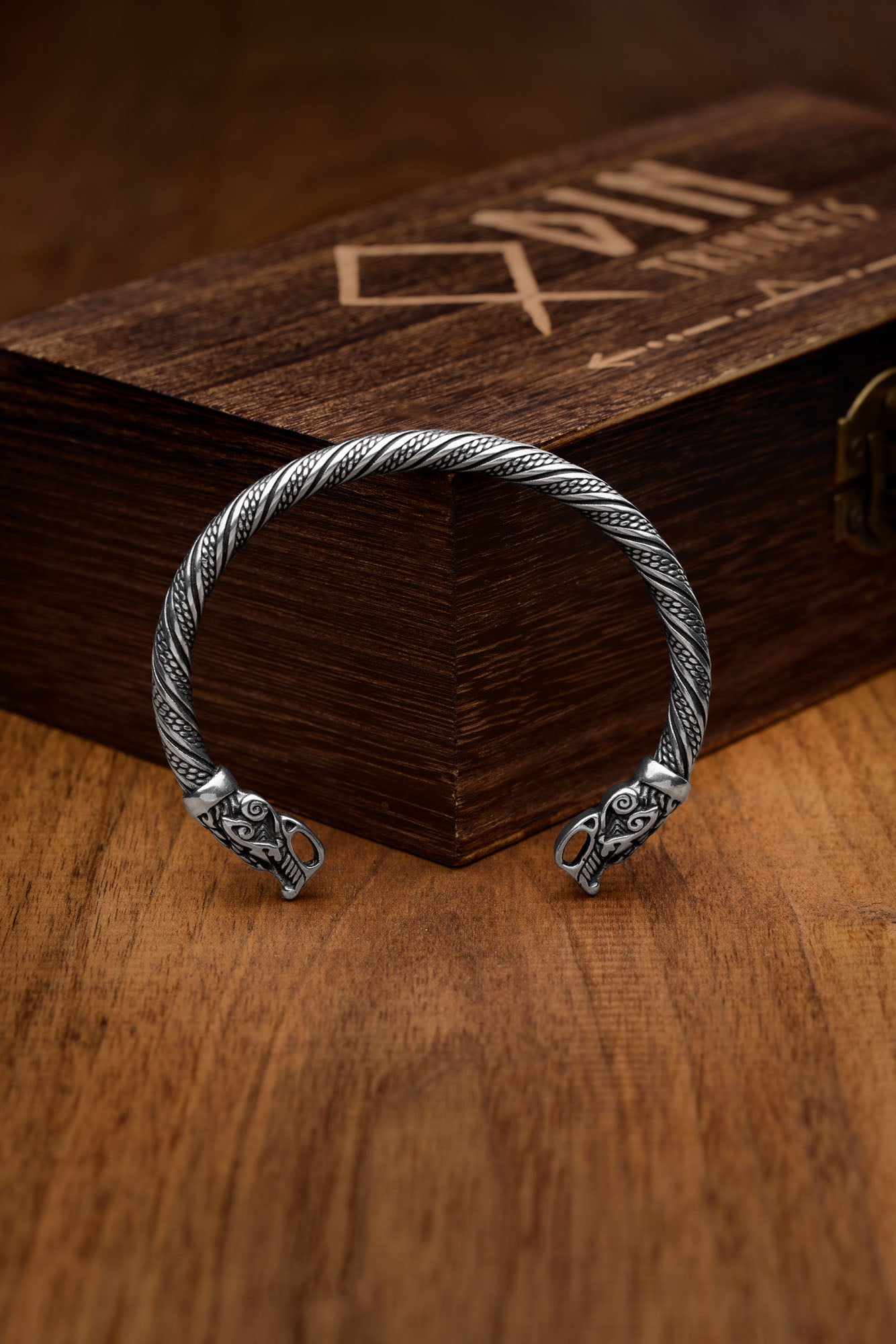 wisted stainless steel bracelet featuring detailed wolf head designs symbolizing Geri and Freki, Odin's legendary wolves, displayed elegantly against a wooden box with the Odin Trinkets logo. A striking piece inspired by Norse mythology.