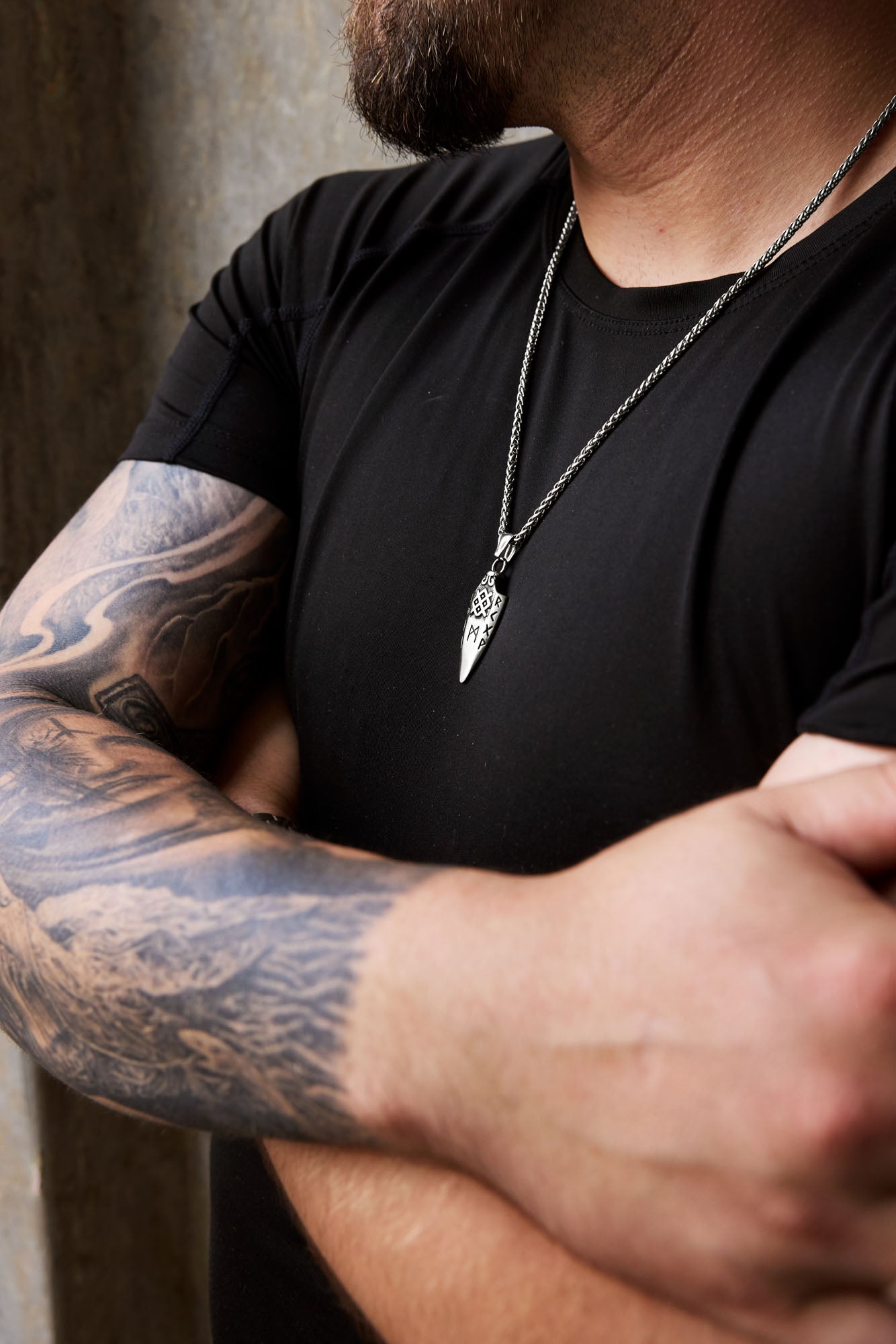 Man wearing the Gungnir necklace with a spearhead pendant engraved with Nordic runes, paired with a tattooed arm and a black shirt, showcasing Norse mythology-inspired jewelry. Available at Odin Trinkets.