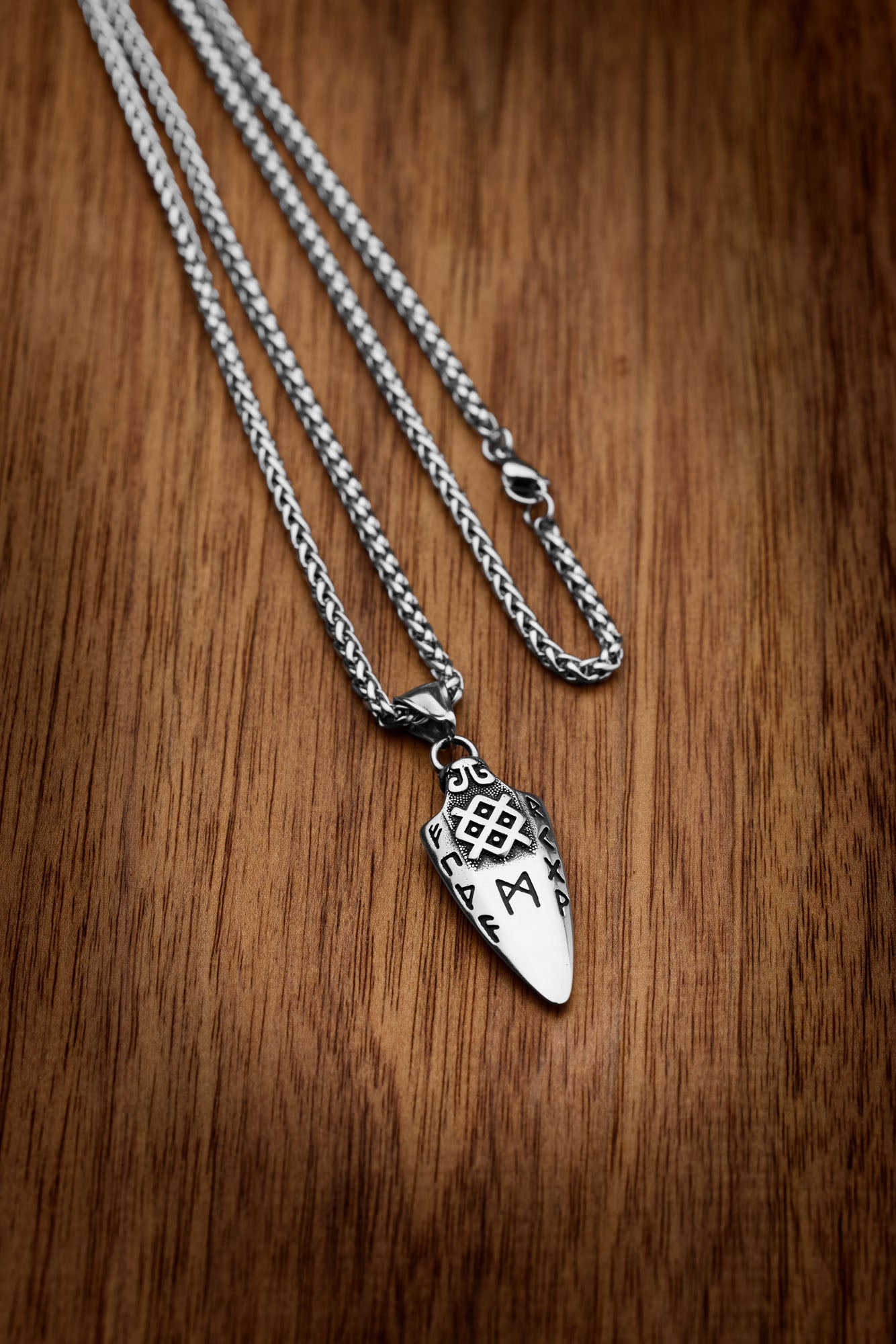 Gungnir necklace featuring a silver pendant shaped like Odin's legendary spear, engraved with Nordic runes, displayed on a wooden surface. Available at Odin Trinkets.