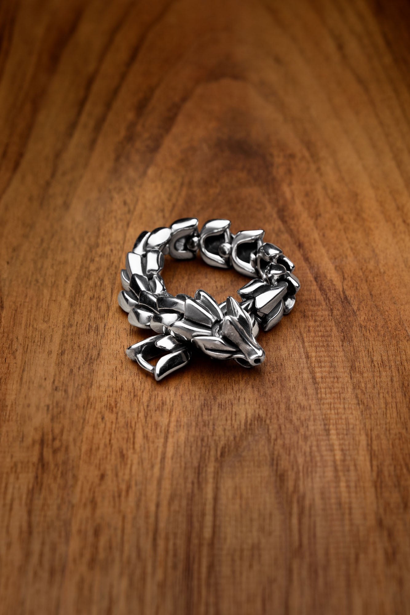 Jormungand bracelet featuring a bold serpent-inspired design, with a detailed snake head clasp, symbolizing the World Serpent from Norse mythology, displayed on a wooden surface. Available at Odin Trinkets.