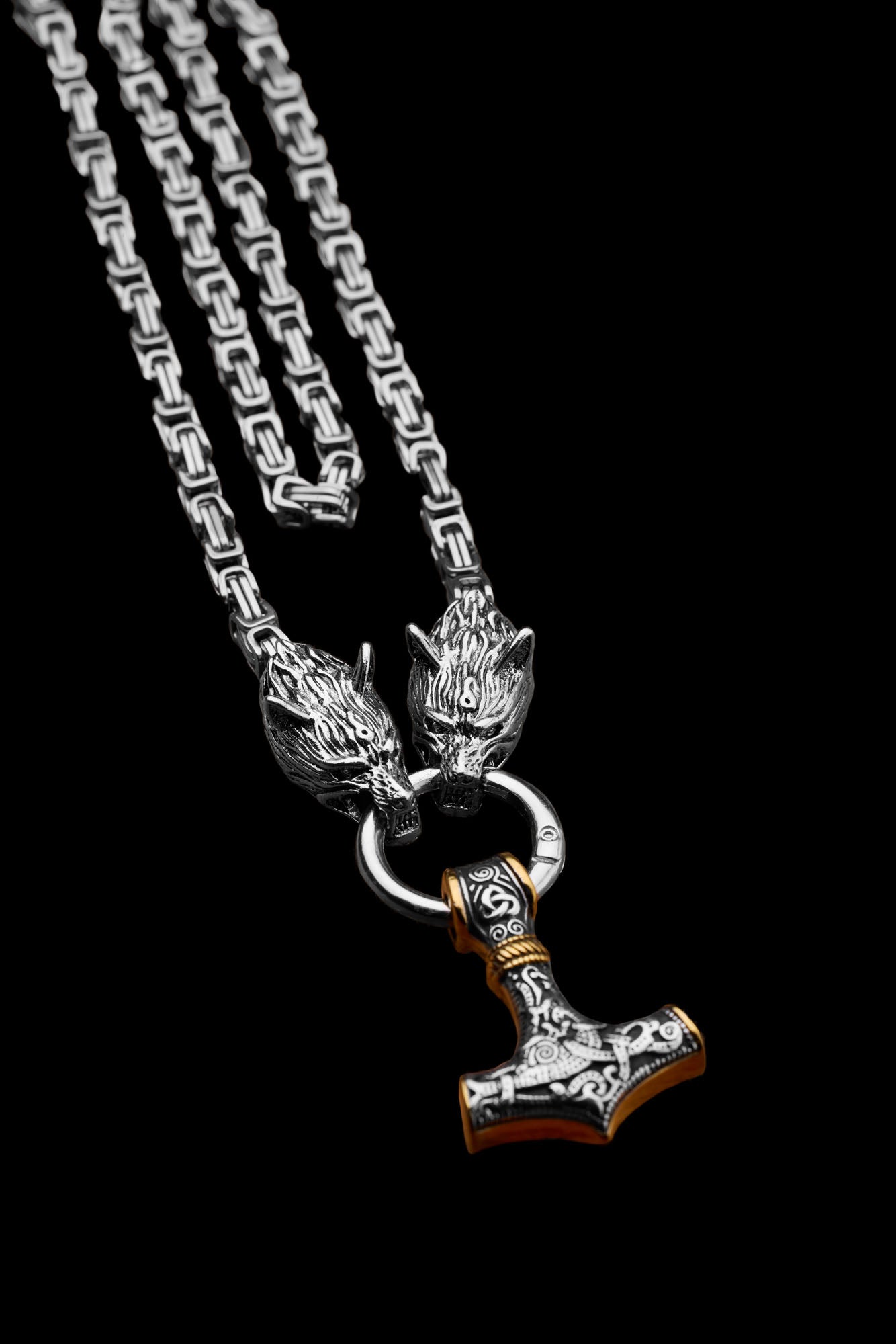 Mjölnir necklace with a Thor's Hammer pendant featuring intricate engravings and gold accents paired with a king chain and wolf head clasps representing Geri and Freki the legendary wolves from Norse mythology displayed on a black background Available at Odin Trinkets