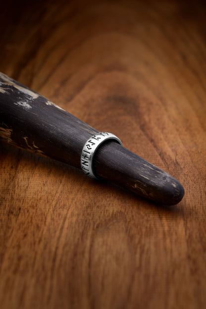 An S925 sterling silver ring engraved with the Elder Futhark alphabet, displayed on a decorative wooden drinking horn. The ring showcases the ancient runes, symbolizing wisdom, protection, and connection to Norse heritage