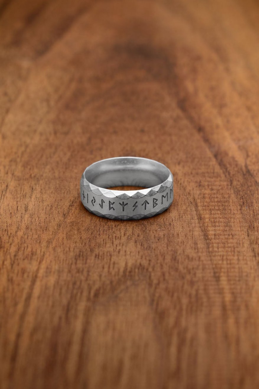 A silver-colored stainless steel rune ring, referred to as the "Silver" variation, showcasing the engraved Elder Futhark alphabet. The faceted texture enhances its modern yet ancient-inspired design, highlighting the mysticism of Norse runes.