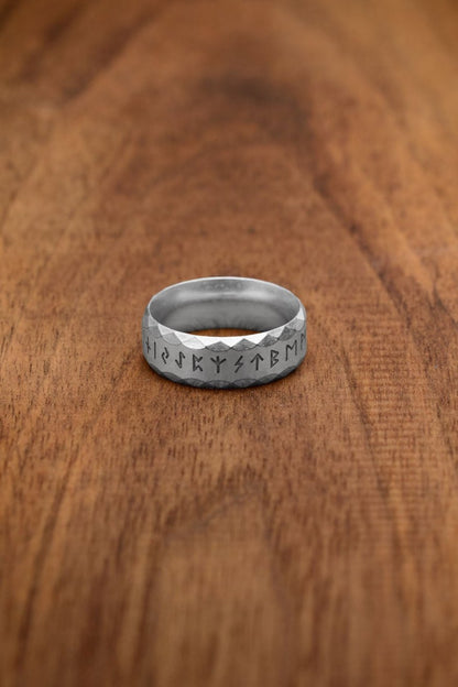 A silver-colored stainless steel rune ring, referred to as the "Silver" variation, showcasing the engraved Elder Futhark alphabet. The faceted texture enhances its modern yet ancient-inspired design, highlighting the mysticism of Norse runes.