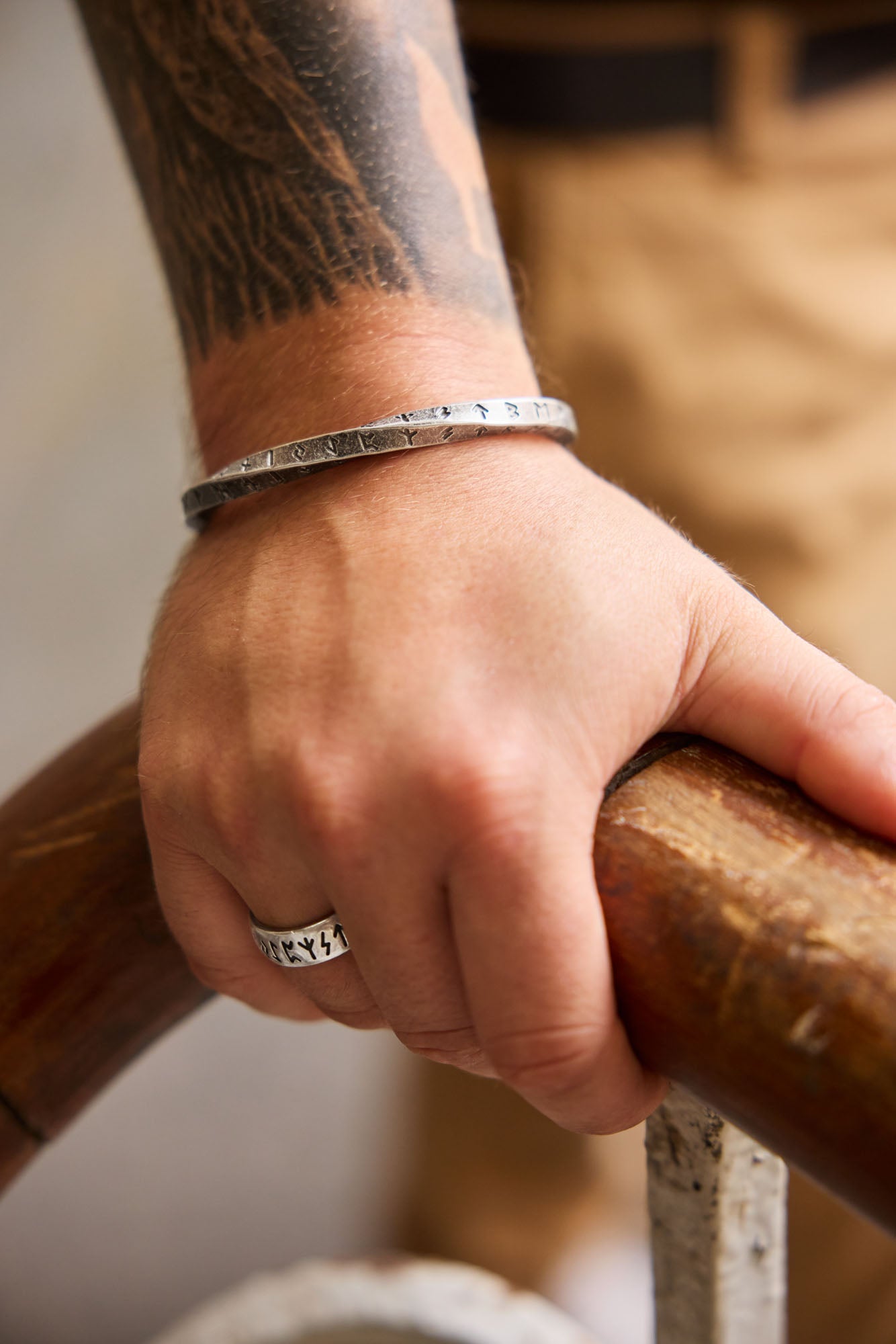 A close-up of a hand wearing a twisted square design cuff bracelet engraved with the Elder Futhark runes and a silver rune ring featuring the same ancient script, showcasing a Viking-inspired accessory set from Odin Trinkets.