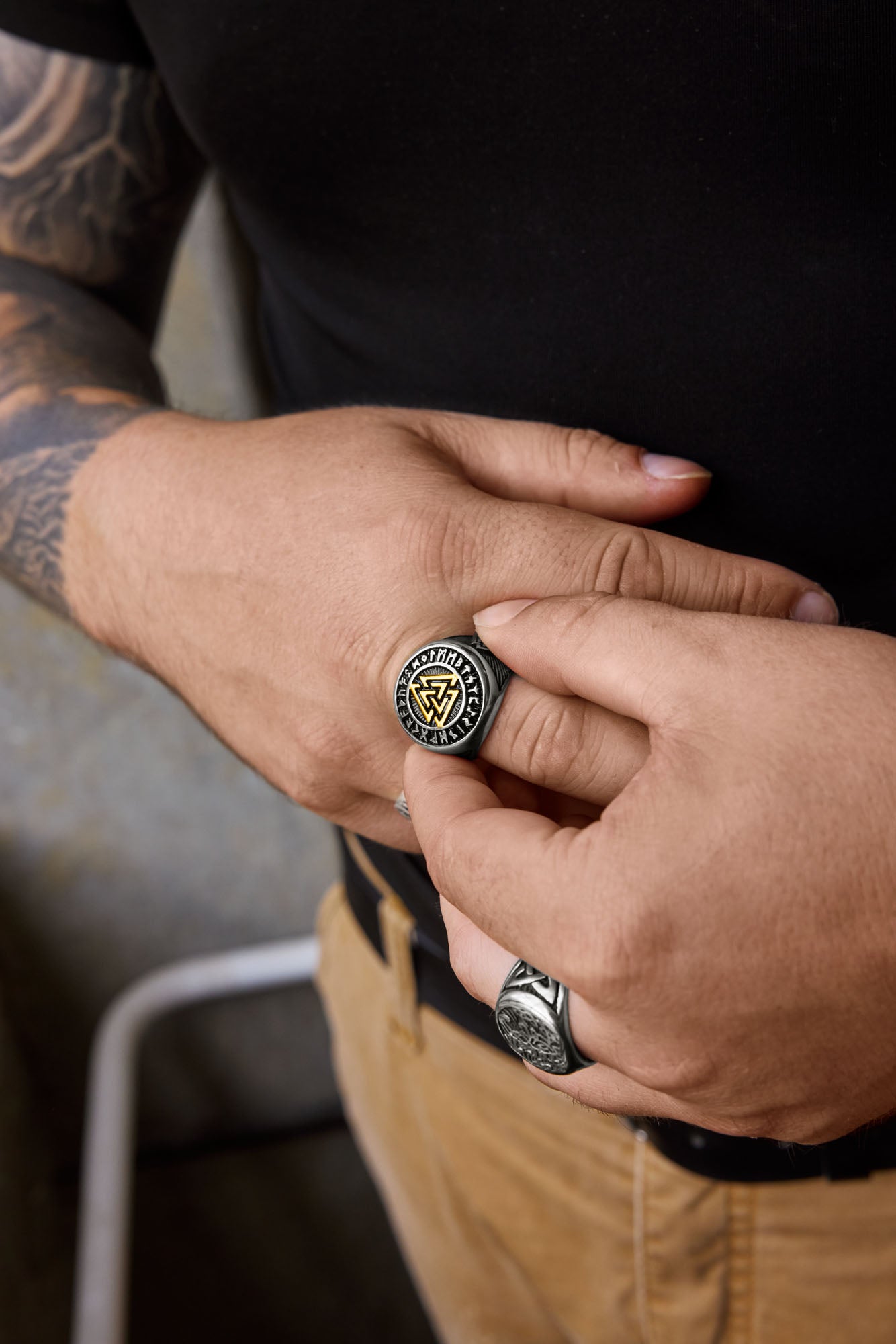 A close-up of hands showcasing the Valknut ring with a gold-accented Valknut symbol encircled by Elder Futhark runes, alongside a Yggdrasil ring with intricate tree of life engravings. Both rings are Norse-inspired designs available at Odin Trinkets.